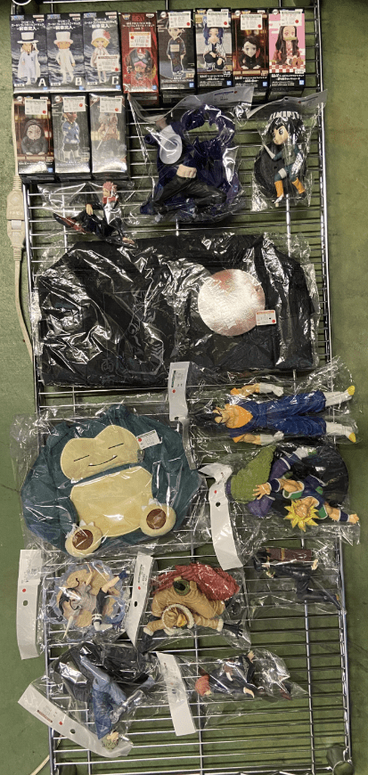 Ver Fotos Recientes 20 - Articulos Japan (post Box Japan) Metal wire display rack with boxed anime figures on the top row and assorted plush toys and character outfits in plastic bags on the lower shelves. Articulos Japan (Post Box Japan)