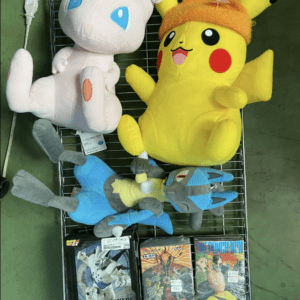 Yellow Pikachu plush with an orange hat sits on a wire rack next to a white Mew plush; three game boxes lie at the bottom.