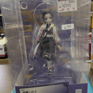 Shinobu Kocho figure from Demon Slayer in a clear acrylic box on a purple base, wearing butterfly-patterned attire. A price tag is visible on the upper right of the box.