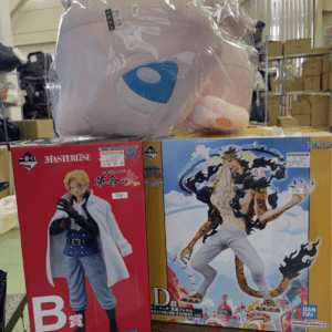 Giant pink plush toy in plastic wrap resting on two One Piece Masterlise boxes in a warehouse setting.