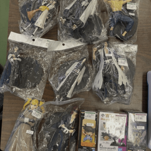 Assorted anime action figures in plastic bags laid out on a table, with price tags visible on each bag.