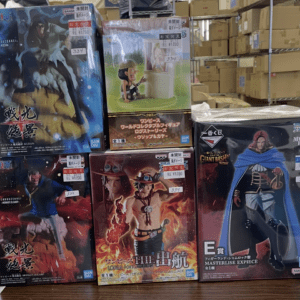 Stack of six Bandai One Piece figurine boxes on a table in a warehouse store, featuring dynamic character artwork and price tags visible on some boxes.
