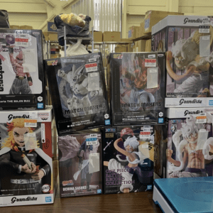 Stacked boxes of anime figures in a store display, featuring Dragon Ball Grandista and One Piece characters.