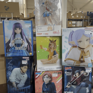 Stacked boxes of anime figure collectibles on a shop floor, with a tall boxed figure in the center and various character boxes around it.