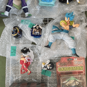 Collection of Dragon Ball Z action figures on bubble wrap, arranged on a metal rack (includes a blue-haired Super Saiyan, green-haired character, and others).