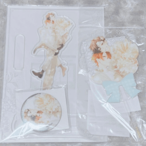 Anime couple illustration merchandise: two clear standees, a circular pin, and sticker sheets featuring a couple embracing in soft colors.
