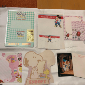 Assorted Mickey Mouse and Snoopy stationery items laid out on a white table, including notebooks, envelopes, and character cutouts.