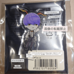 Sticker of a small anime-style character with purple hair in overalls, attached to a sealed black plastic package with a barcode on a cardboard backing.
