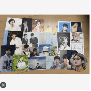A spread of glossy photo photocards laid out on a wooden floor, featuring multiple male-portrait cards in varied outfits and colors.