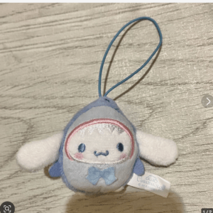 Small pastel-blue plush keychain in the shape of a round, kawaii creature with a white face and blue bow tie, looped for attaching to bags or keys