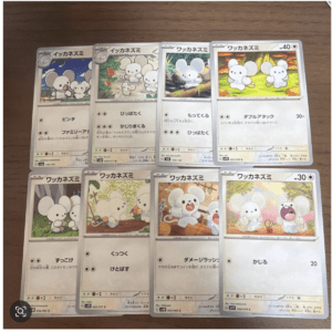 Eight Pokémon cards featuring a small white mouse-like creature in different scenes, laid out on a wooden surface in protective sleeves.