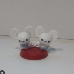 Two small white bunny figurines with large ears standing on a red circular base on a pale surface, facing the camera.