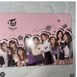 Group photo of nine young women posing together on a pink backdrop with doodles and a logo, likely a pop group promotional poster.