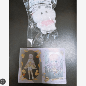 Plastic-wrapped white plush toy with a label above two anime-style character cards on a dark table surface.