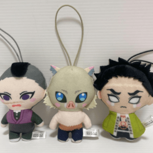 Three chibi plush keychains hanging on cords: left a grey-haired figure in purple, center a pig‑like creature with blue eyes, right a black-haired figure in a green jacket.  Articulos Japan (Post Box Japan)
