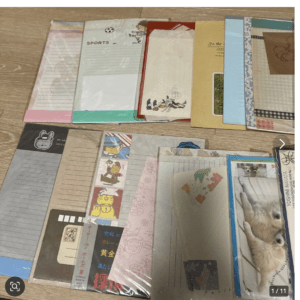Assorted colorful folders and decorative envelopes spread out on a wooden floor, viewed from above.