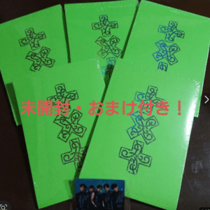 Five bright green booklets with black cross logos, fanned out on a surface; red Japanese text overlays the image with a small group photo at the bottom.