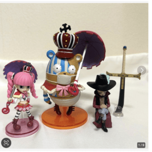 Three collectible figures: a pink-haired girl with a staff, a crown-wearing cake-like figure with a pink parasol, and a seated gunslinger beside a decorative sword on a white surface.