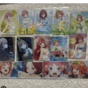 Assorted anime character trading cards in protective sleeves laid out on a light surface, each card showing a different female character in colorful outfits.