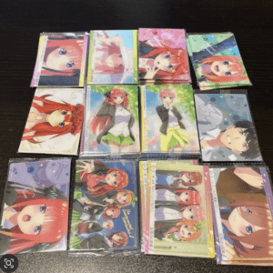 Plastic-wrapped anime trading cards with colorful character art laid out in a 4x3 grid on a dark table, featuring red-haired and other cheerful characters.