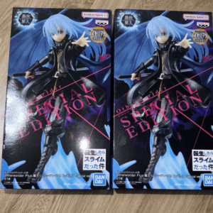 Two boxed anime figure boxes with a blue-haired character in a black coat holding a sword, placed on a wooden surface.