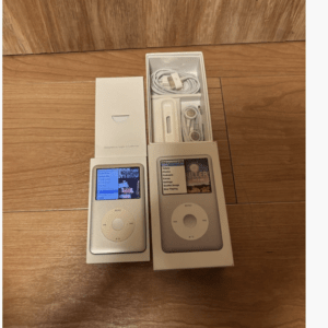Two white iPod music players in their boxes with USB cables and earphones laid out on a wooden floor.