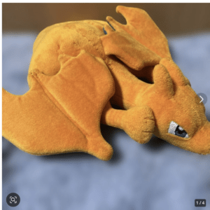 Orange plush dragon toy resting on its side against a blue background.