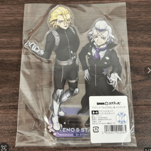 Package containing an acrylic stand figure of two Dr. Stone characters in black outfits, sealed in plastic on a wooden surface.