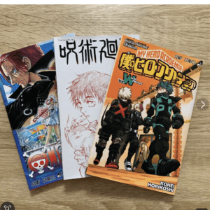 Three manga volumes fanned on a wooden table; rightmost is My Hero Academia with armored heroes.