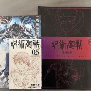 Collage of manga volumes on a gray surface: a white cover with a drawn male character, blue-toned art, and a black volume with a pink band reading Start Guide & Art Works.