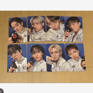 Eight photo cards of K-pop group members in white jackets wearing safety glasses, each holding a small black toy gun on a wooden floor.
