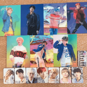 Collection of glossy K-pop photo cards and posters laid out on a cork floor: six large portrait posters in a row on top, with a row of mid-sized photos beneath and a line of smaller cards along the bottom, featuring young male performers in colorful outfits.