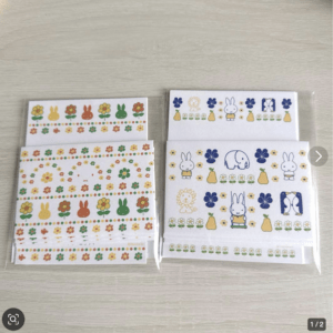 Sets of decorative sticker sheets featuring colorful bunnies, flowers, and pumpkins in a rainbow of colors, laid on a light wood surface (in plastic packaging).