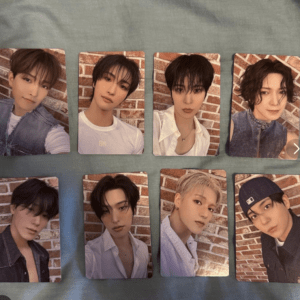 Eight photo cards of a K-pop group arranged in two rows on a teal surface, each member posing against a brick wall backdrop.