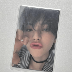 Close-up selfie of a young person with pouty lips, touching the camera, wearing a black choker and a checkered shirt.