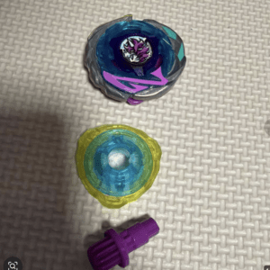 Two colorful spinning tops (Beyblade) on a woven surface, with a purple launcher below them.