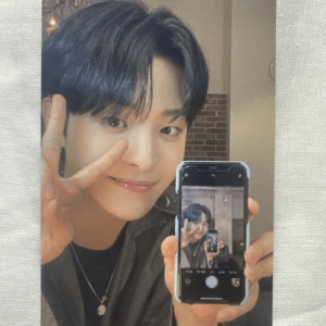 Smiling person with short black hair making a peace sign while taking a mirror selfie with a phone.