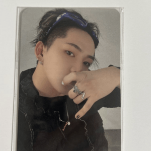Person posing for a selfie, wearing a black jacket, silver rings, a necklace, and a blue headband in their hair, hand near face.