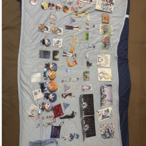 Assorted anime figures, cards, and merch laid out on a blue quilted bedspread as a collection display.