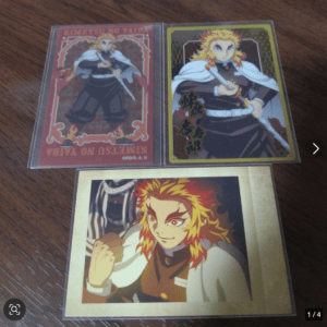 Three Demon Slayer trading cards on a wooden table, each showing Flame Hashira Kyojuro Rengoku in different poses with flames in his hair (red/gold borders).