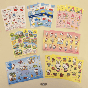 Assorted Hello Kitty and friends sticker sheets and decorative cards laid out on a light surface, featuring pink, blue, and yellow themes.