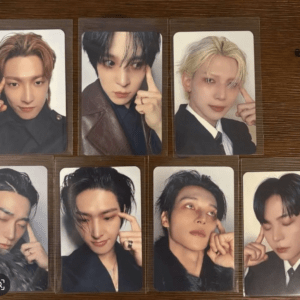 Seven glossy photo cards featuring male K-pop idols arranged on a wooden surface, each in a portrait pose with different hairstyles and outfits.