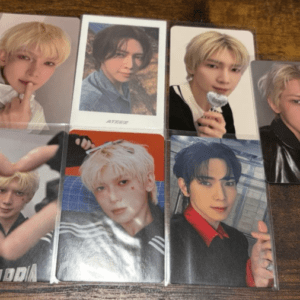 Collection of eight glossy photo cards laid on a wooden surface, each depicting a young man with various hairstyles in different poses and outfits.