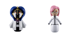 Two small toy figures facing forward: left figure in a blue hood and purple cape; right figure with pink hair and a white dress.