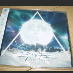 CD case with a sci‑fi style cover: a large bright moon above a snowy city, framed by a glowing triangle, with the title 'FAKE' and Japanese text on the spine/cover.  Articulos Japan (Post Box Japan)