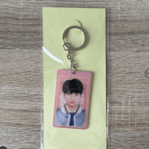 Keychain featuring a pink ID card with a young man in a blue school uniform, attached to a metal ring, on a pale yellow backing.