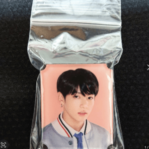 Pink background photo card featuring a young man with black hair in a gray jacket and blue tie, sealed in a resealable plastic bag (collectible card).
