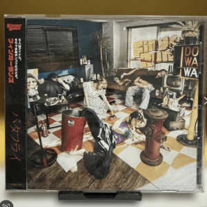 CD jewel case featuring a retro living room scene with several people lounging and playing, a checkered orange-and-white floor, and bold text on the left side of the case  Articulos Japan (Post Box Japan)