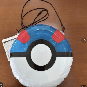 Inflatable Poké Ball-shaped accessory with a black string strap on a wooden table, blue top, red accents, and white bottom.