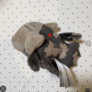 Camo-patterned plush animal with floppy ears and a red eye, tag shows Pokémon Center.  Articulos Japan (Post Box Japan)